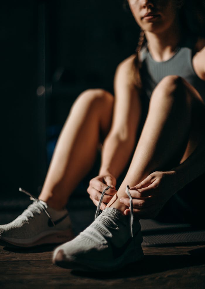 Woman preparing for workout by tying shoelaces in a gym, emphasizing fitness and sport.